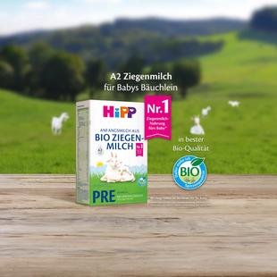Packung HiPP Bio Ziegenmilch PRE mit Bio-Siegel auf Holztisch vor grüner Landschaft mit Ziegen im Hintergrund