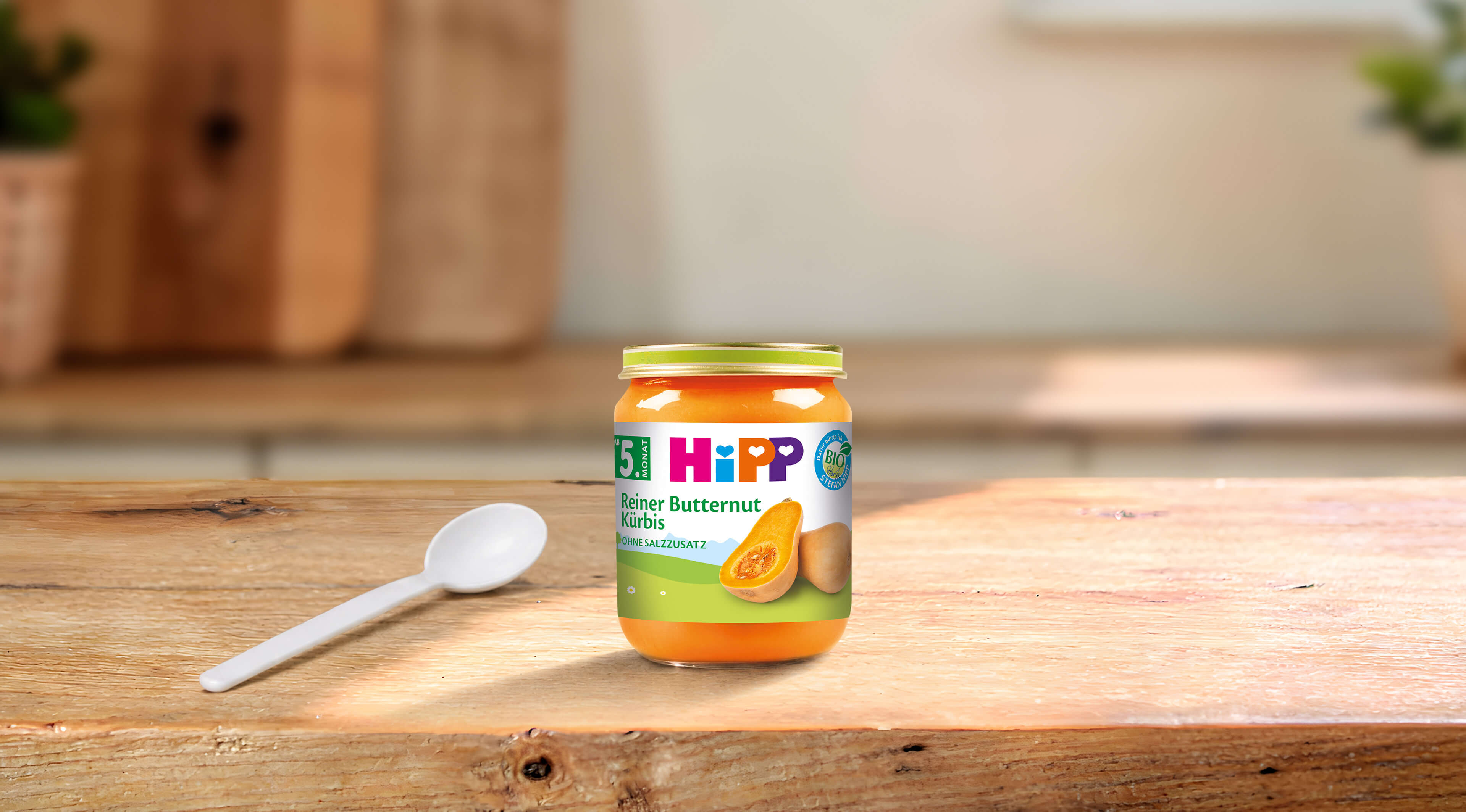 HiPP Bio-Gläschen „Reiner Butternut Kürbis“ ab dem 5. Monat mit Löffel auf Holztisch in heller Küche
