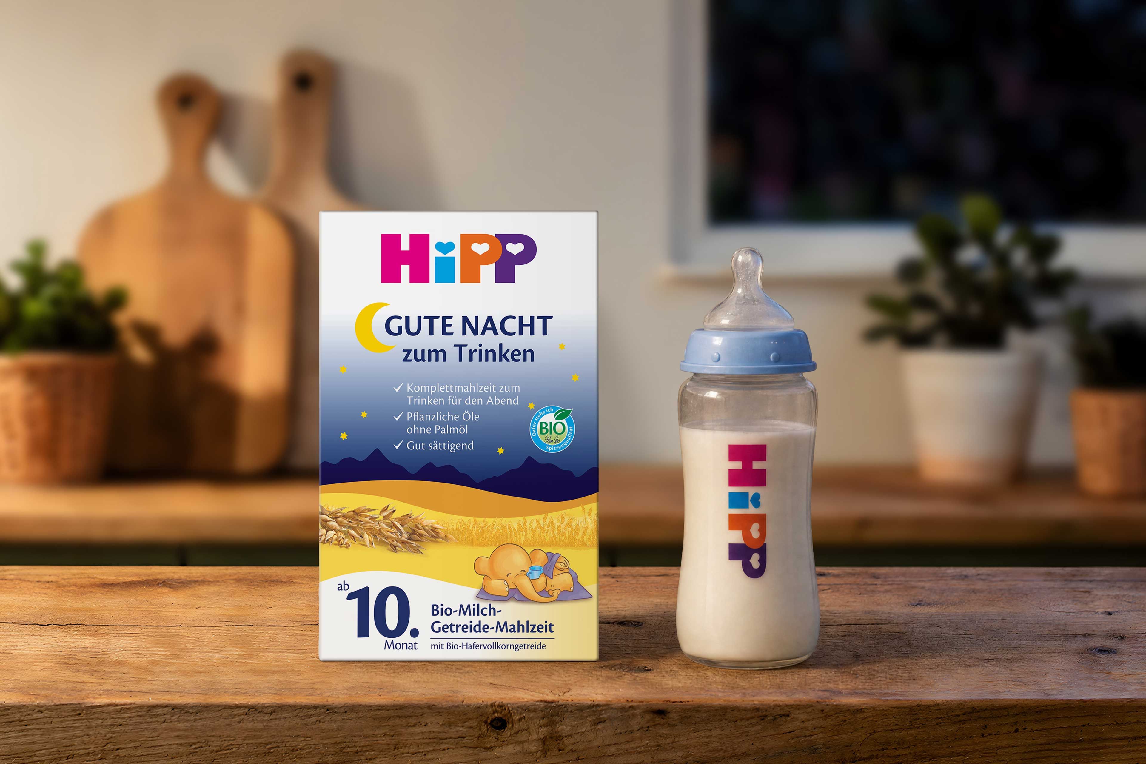 HiPP Gute Nacht Bio-Milch-Getreide-Mahlzeit Packung mit Babyflasche auf Holztisch in gemütlicher Abendküche