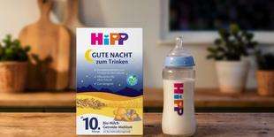 HiPP Gute Nacht Bio-Milch-Getreide-Mahlzeit Packung mit Babyflasche auf Holztisch in gemütlicher Abendküche