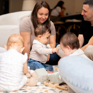 Three babies playing together on play mat with parents watching them