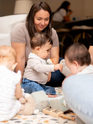 Three babies playing together on play mat with parents watching them