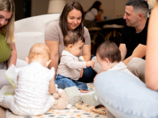 Three babies playing together on play mat with parents watching them
