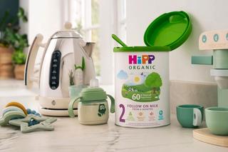 HiPP Organic follow on milk powder tin open with scoop next to a kettle and baby bottle of milk