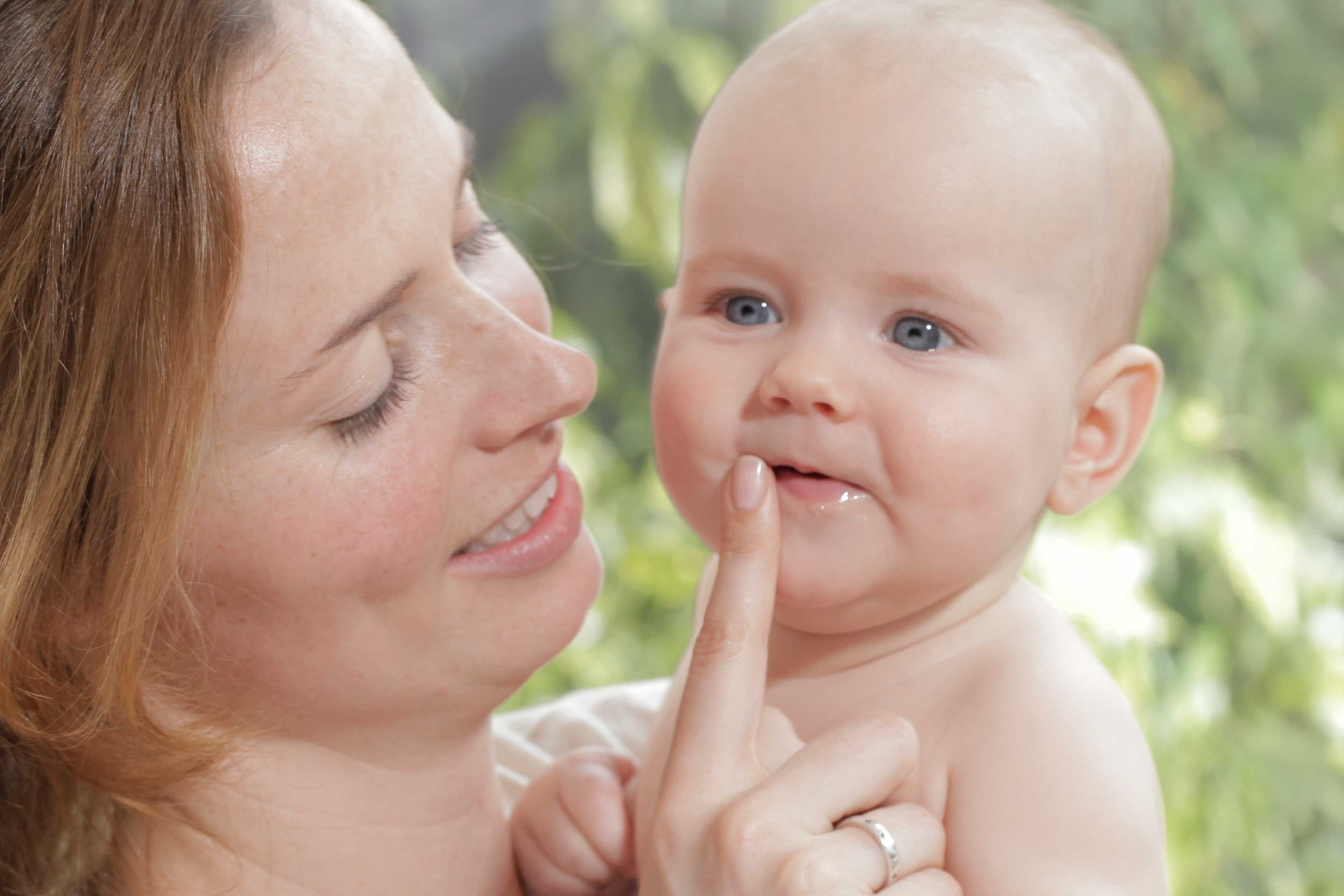 Frau hält lächelnd ein Baby und berührt mit dem Zeigefinger dessen Lippen