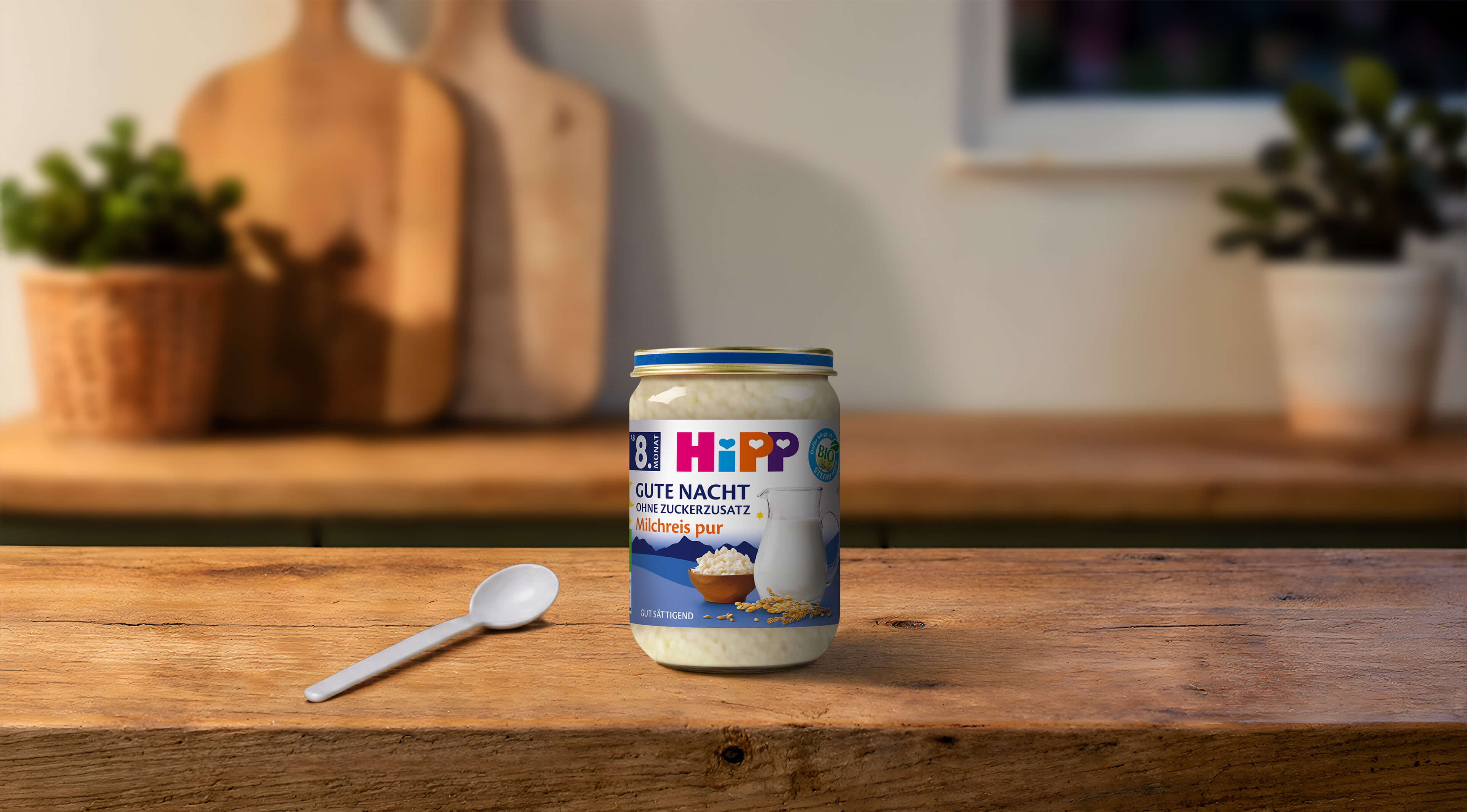 HiPP Gute Nacht Milchreis pur Bio-Abendbrei im Glas mit Löffel auf einem Holztisch in gemütlicher Küchenatmosphäre