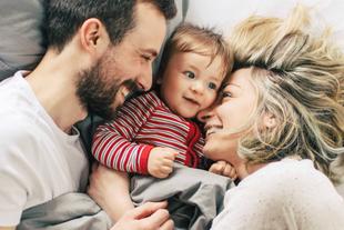 Ein zärtlicher Moment zwischen einer Mutter und ihrem Baby, in dem die Mutter das Baby sanft anschaut, während beide auf einem Bett liegen.