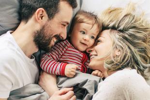 Ein zärtlicher Moment zwischen einer Mutter und ihrem Baby, in dem die Mutter das Baby sanft anschaut, während beide auf einem Bett liegen.