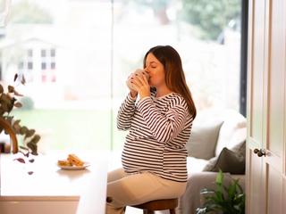 Pregnant woman sat drinking tea at breakfast bar