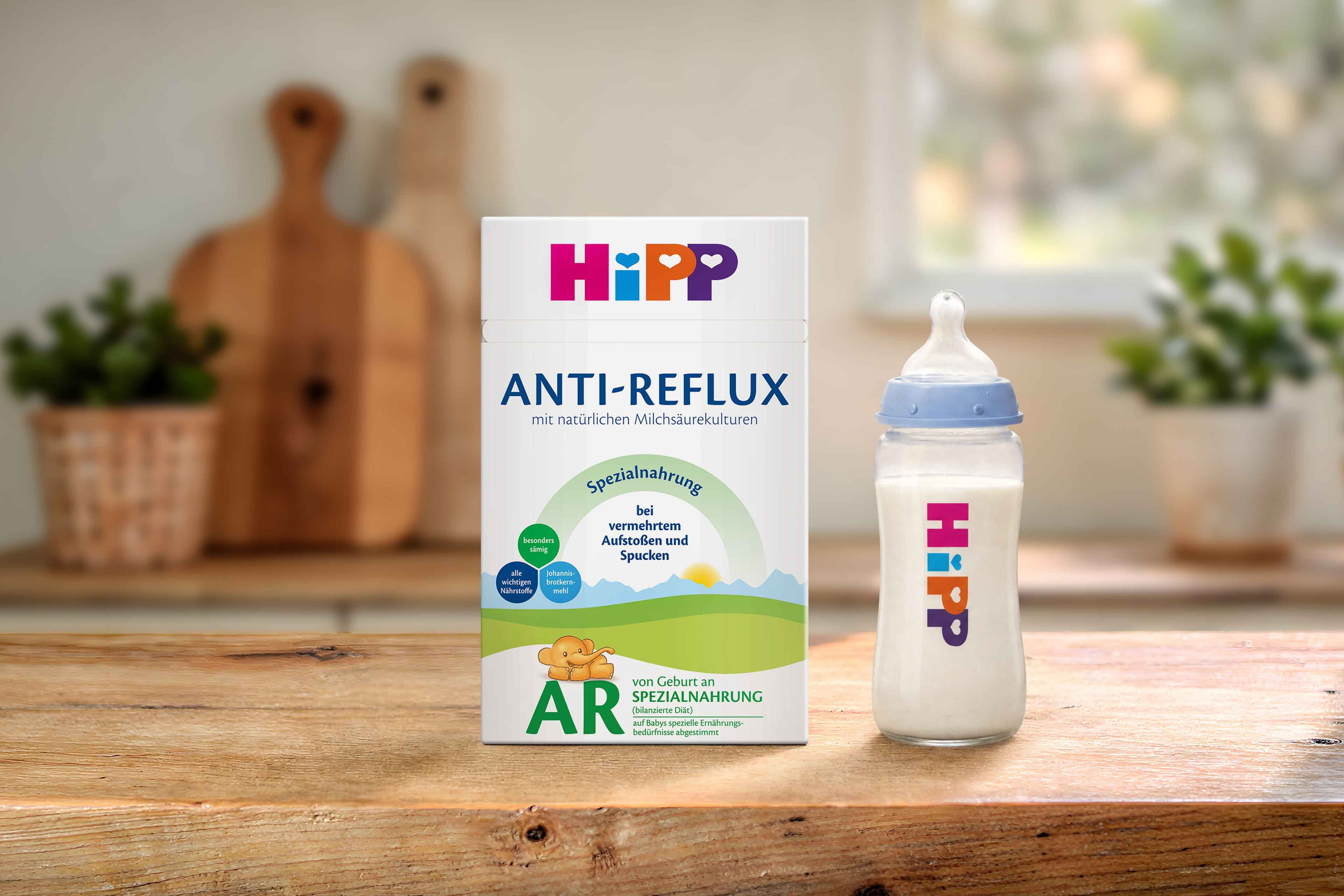 HiPP Anti-Reflux Spezialnahrung Packung und gefülltes Babyfläschchen mit HiPP Logo auf einem Holztisch in einer warmen Küchenumgebung
