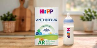HiPP Anti-Reflux Spezialnahrung Packung und gefülltes Babyfläschchen mit HiPP Logo auf einem Holztisch in einer warmen Küchenumgebung