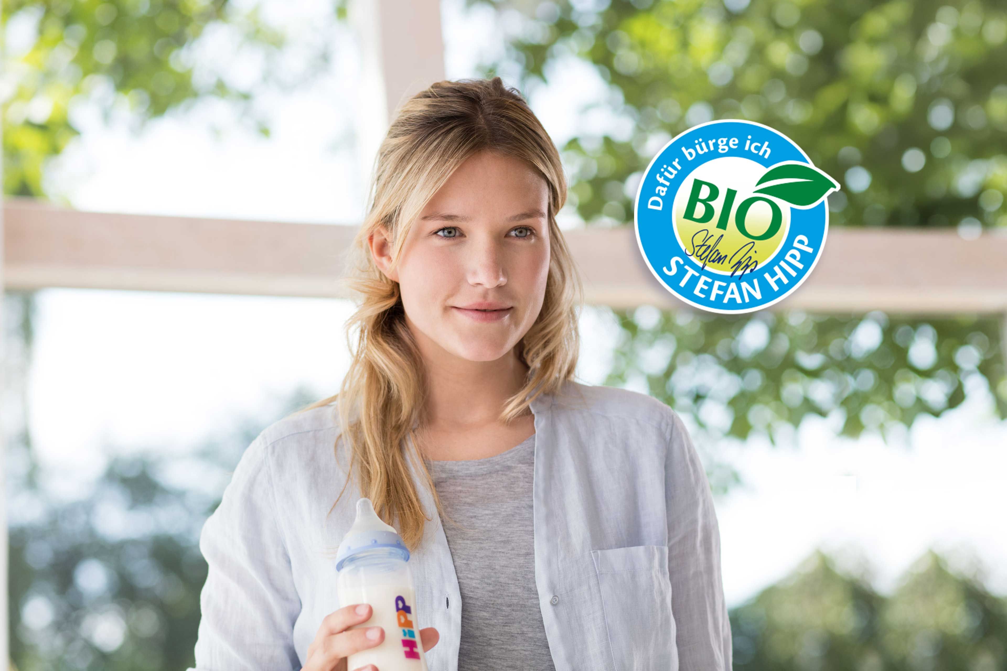 Eine junge Frau, die eine Flasche in der Hand hält, mit einem Logo im Hintergrund, auf dem "BIO" und "Dafür stehe ich" steht, begleitet von einem grünen Blattsymbol.