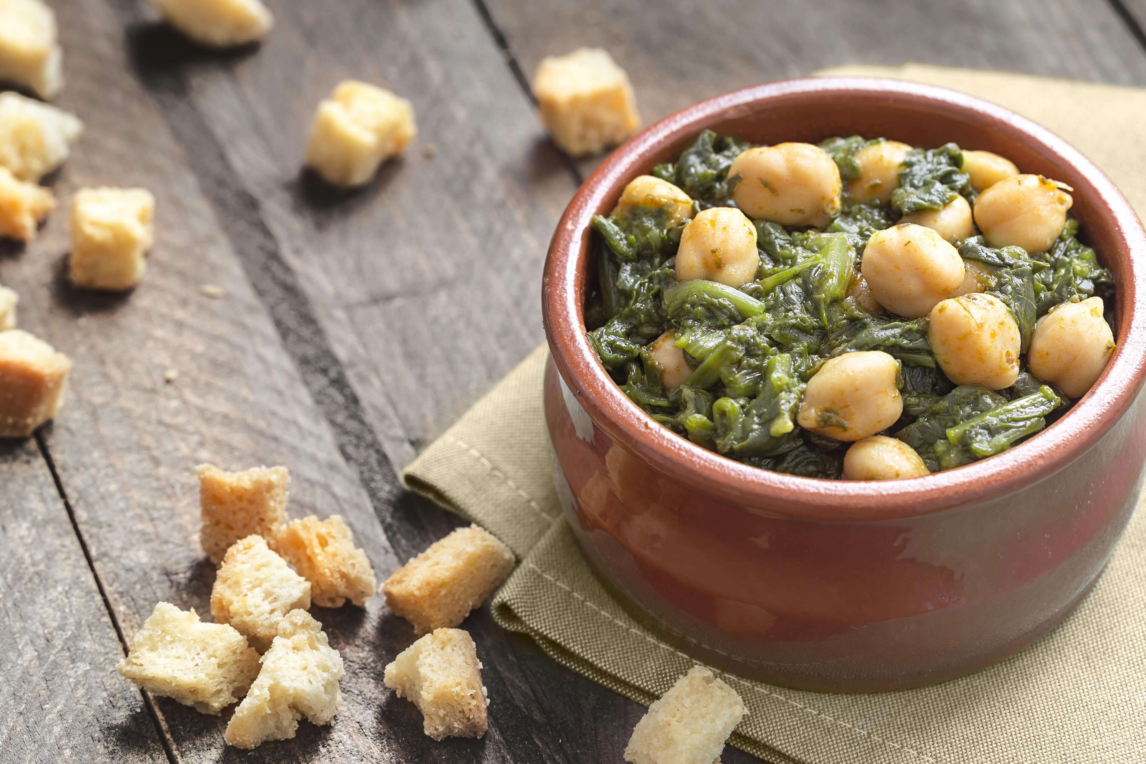 Eine Schüssel mit Kichererbsen, gemischt mit grünem Blattgemüse, dazu Croutons, die in der Schüssel verstreut sind.