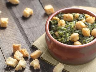 Eine Schüssel mit Kichererbsen, gemischt mit grünem Blattgemüse, dazu Croutons, die in der Schüssel verstreut sind.