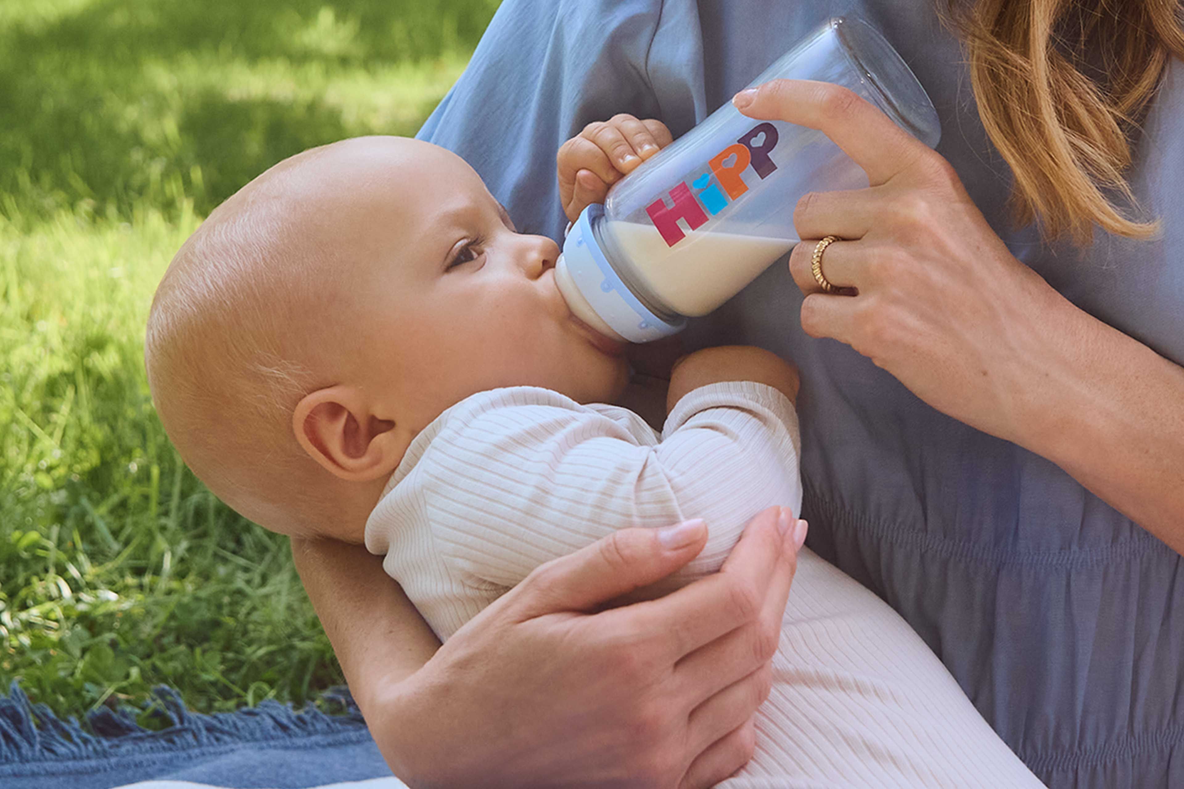 Eine Mutter, die ihr Baby mit der Flasche füttert, im Freien.