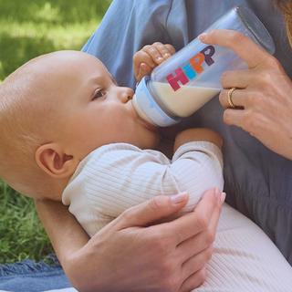 Eine Mutter, die ihr Baby mit der Flasche füttert, im Freien.