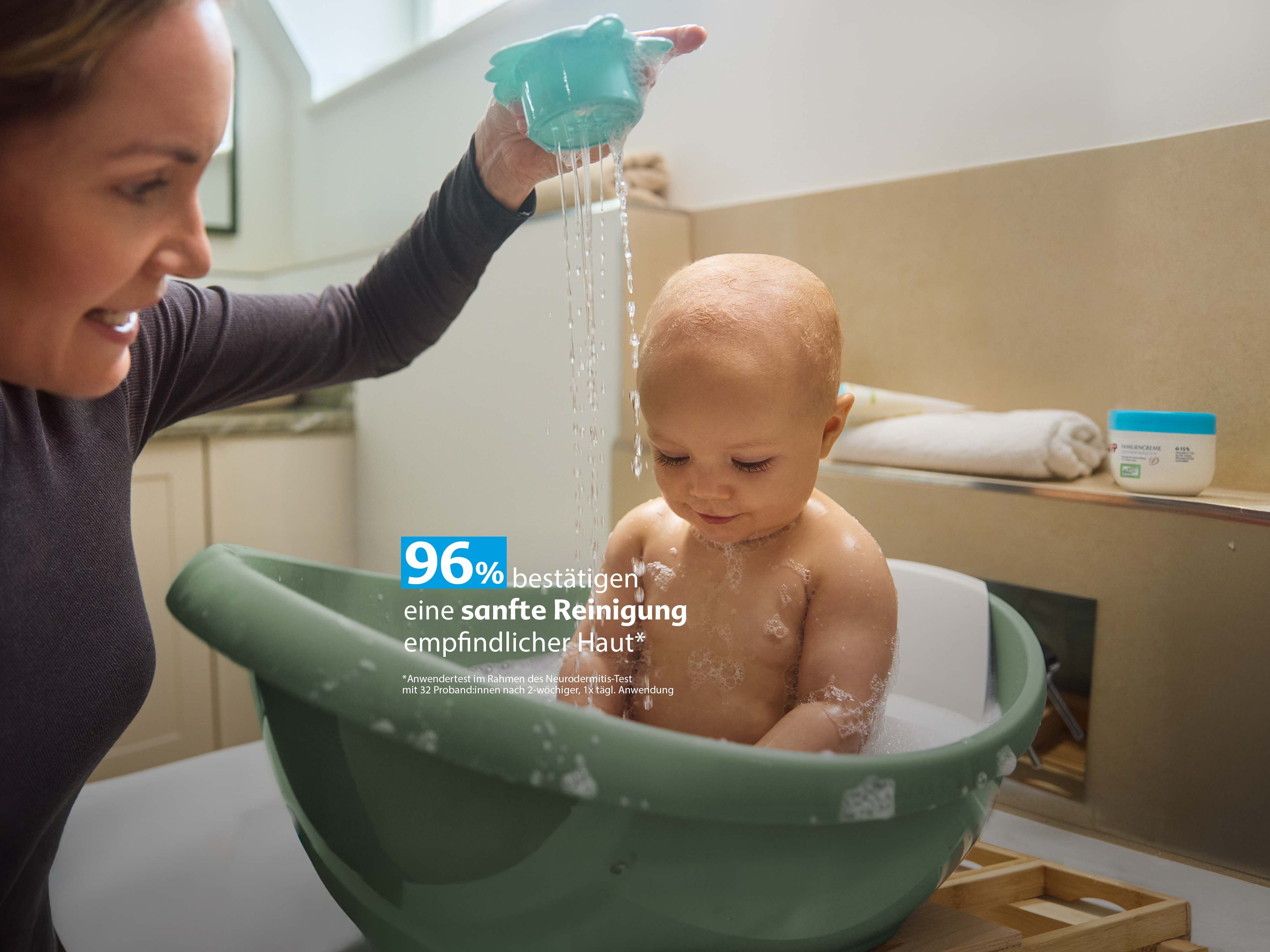 Mutter badet ihr Baby sanft in einer Wanne, Wasser rinnt über den Kopf, Text hebt 96 % Zufriedenheit bei empfindlicher Haut hervor.
