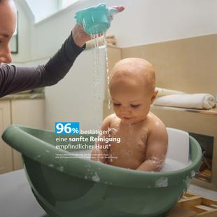 Mutter badet ihr Baby sanft in einer Wanne, Wasser rinnt über den Kopf, Text hebt 96 % Zufriedenheit bei empfindlicher Haut hervor.