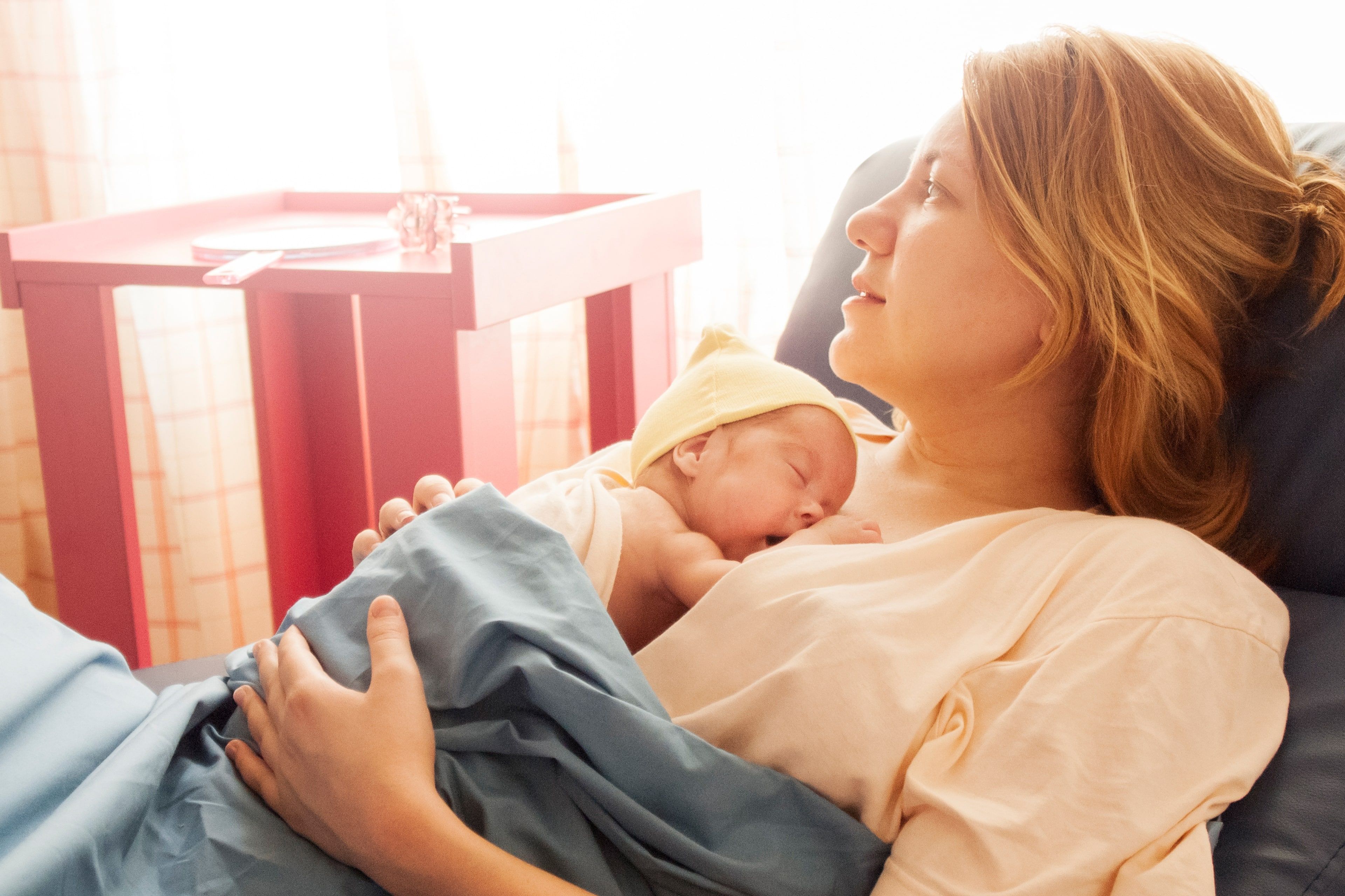 Eine Frau hält ein Baby, beide ruhen sich bequem aus, im Hintergrund ein rosa Tisch.