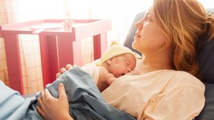 Eine Frau hält ein Baby, beide ruhen sich bequem aus, im Hintergrund ein rosa Tisch.