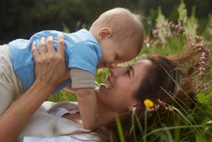 Lachende Mutter spielt mit ihrem Baby auf einer blühenden Wiese und genießt die Natur für eine lebenswerte Zukunft.
