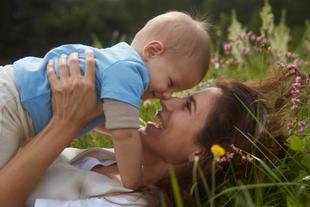 Lachende Mutter spielt mit ihrem Baby auf einer blühenden Wiese und genießt die Natur für eine lebenswerte Zukunft.