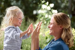 Ein herzerwärmender Moment zwischen einem jungen Mädchen und einer Frau, die sich im Freien spielerisch die Hand geben.