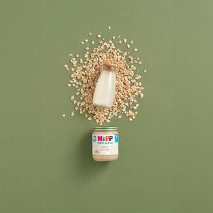 HiPP Organic Creamy Porridge jar with a bottle of milk and scattered oats on a green background