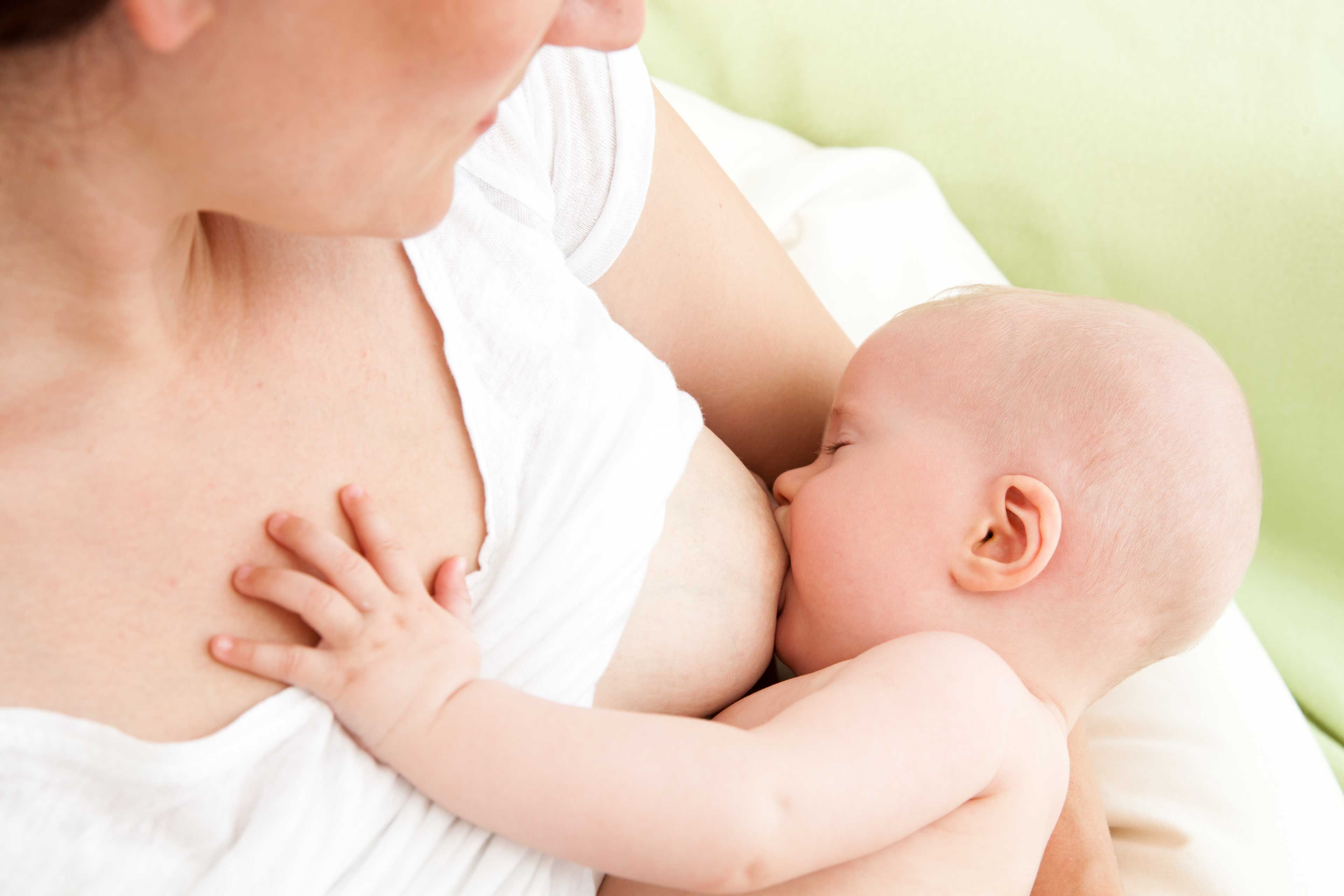 Frau stillt Baby, das mit einer Hand ihre Brust berührt