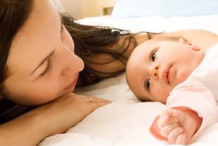 Ein zärtlicher Moment zwischen einer Mutter und ihrem Baby, in dem die Mutter ihr Gesicht sanft neben das des Babys legt und beide einen heiteren und intimen Moment zu teilen scheinen.