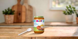 HiPP Bio Babygläschen „Spätzle mit Gulasch“ ab 8. Monat auf Holztisch, daneben ein Löffel in heller, gemütlicher Küche