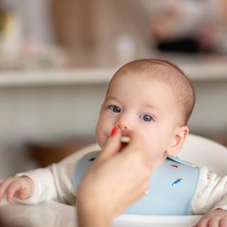 Little boy eating baby food off of spoon being fed to him by a parent