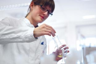 Laborantin im weißen Kittel prüft HiPP Bio Milch im Labor mit Kolben und Pipette unter strengen Qualitätskontrollen.