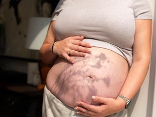 Close up of woman holding her bump with flower shadow across the image