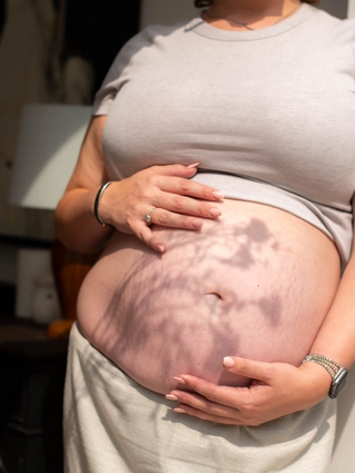 Close up of woman holding her bump with flower shadow across the image