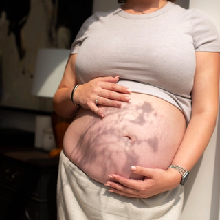 Close up of woman holding her bump with flower shadow across the image