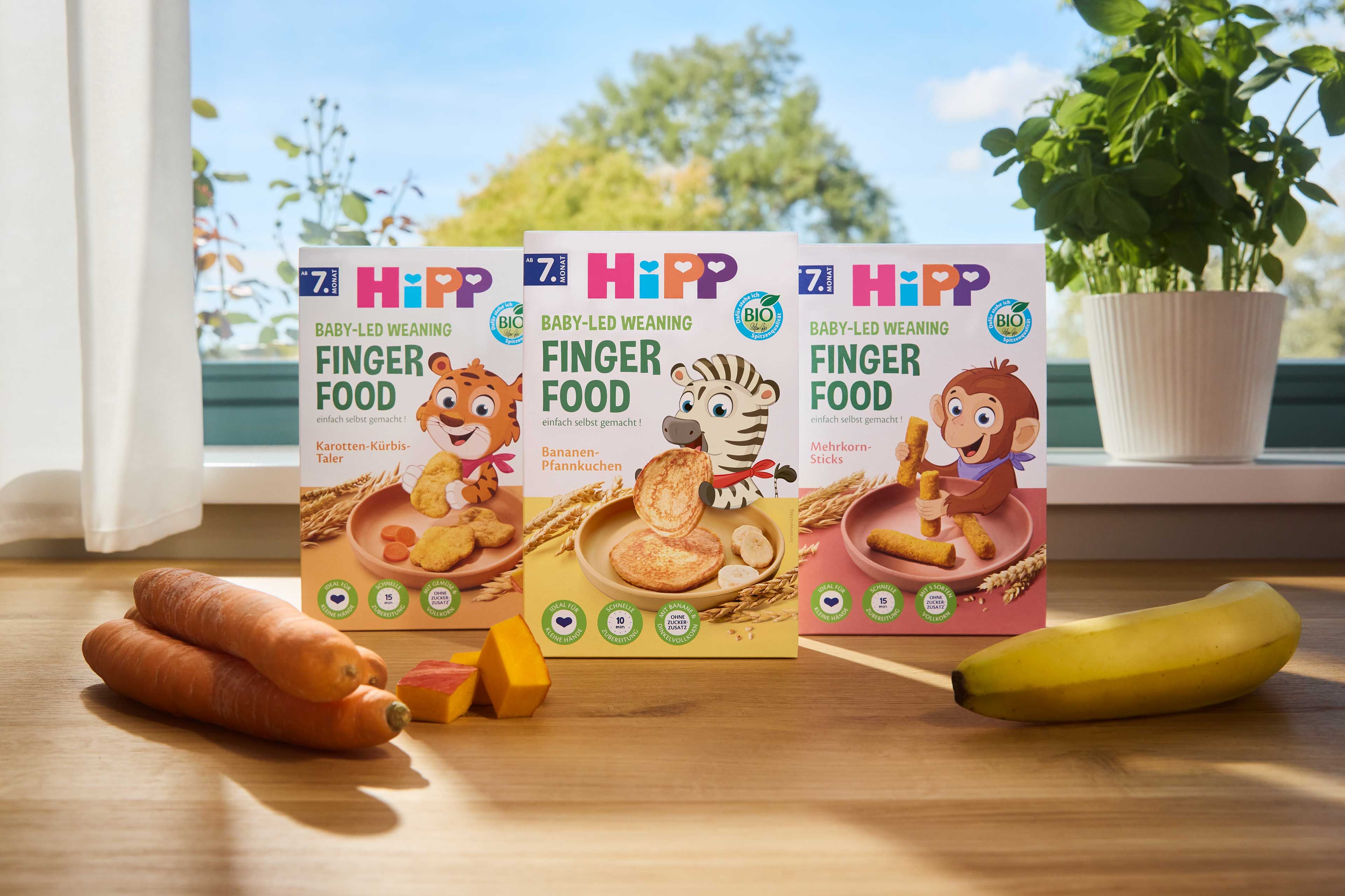 Drei Packungen HiPP Bio Fingerfood ab dem 7. Monat mit Karotten, Kürbis und Banane auf einem Holztisch