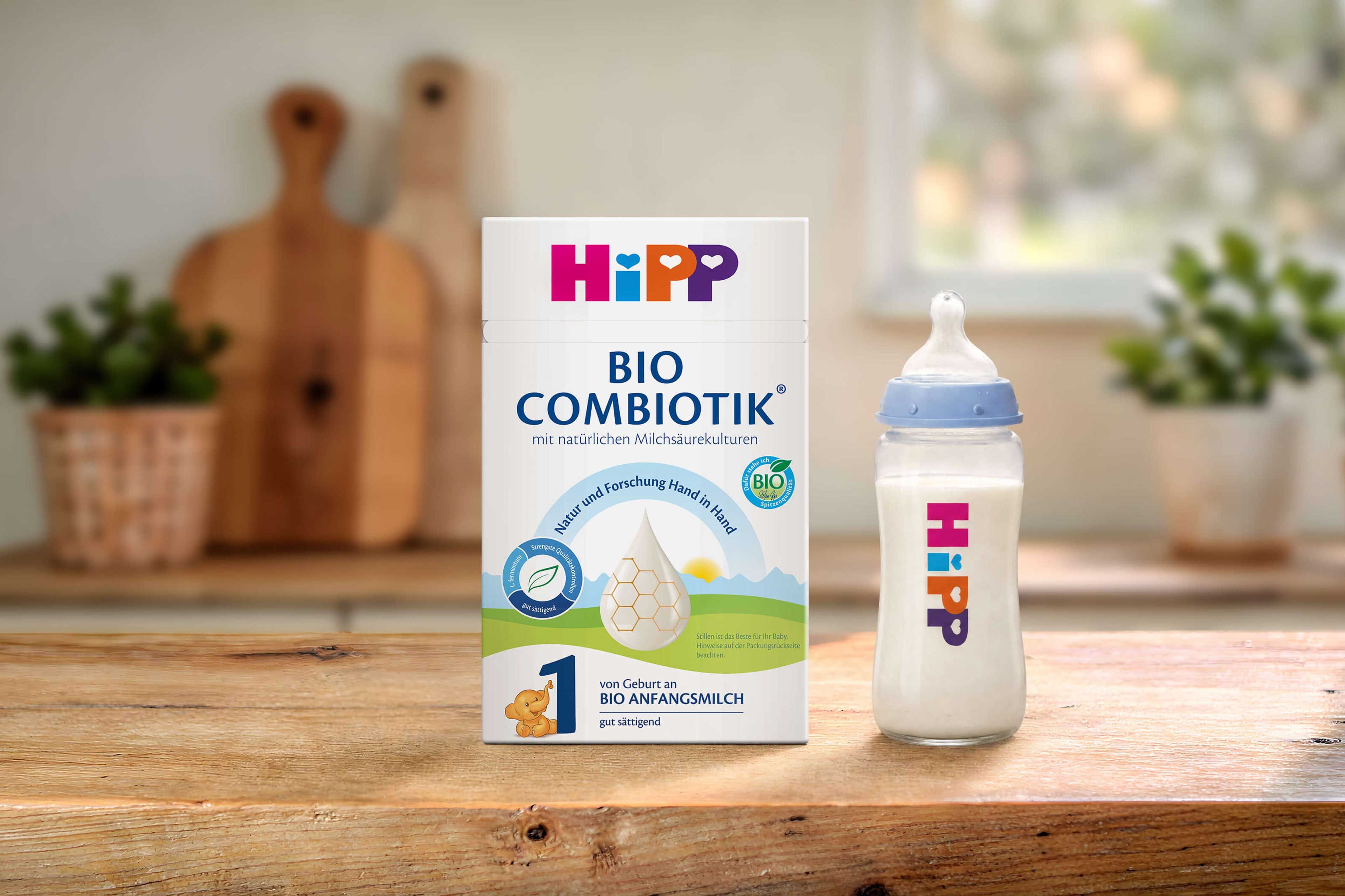 HiPP 1 BIO Combiotik® Anfangsmilch-Packung neben gefülltem HiPP-Babyfläschchen auf Holztisch in heller Küche