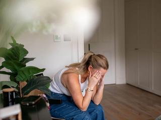 Pregnant woman sitting on a chair at home, head in hands, showing first trimester fatigue and overwhelm.