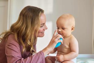 Lächelnde Mutter trägt sanft Familiencreme auf die Nase ihres sitzenden Babys in der Windel auf.