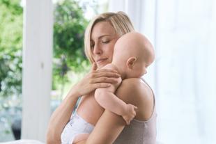 Mutter hält ihr Baby aufrecht an der Schulter und streichelt beruhigend den Rücken, um ein Bäuerchen zu unterstützen.