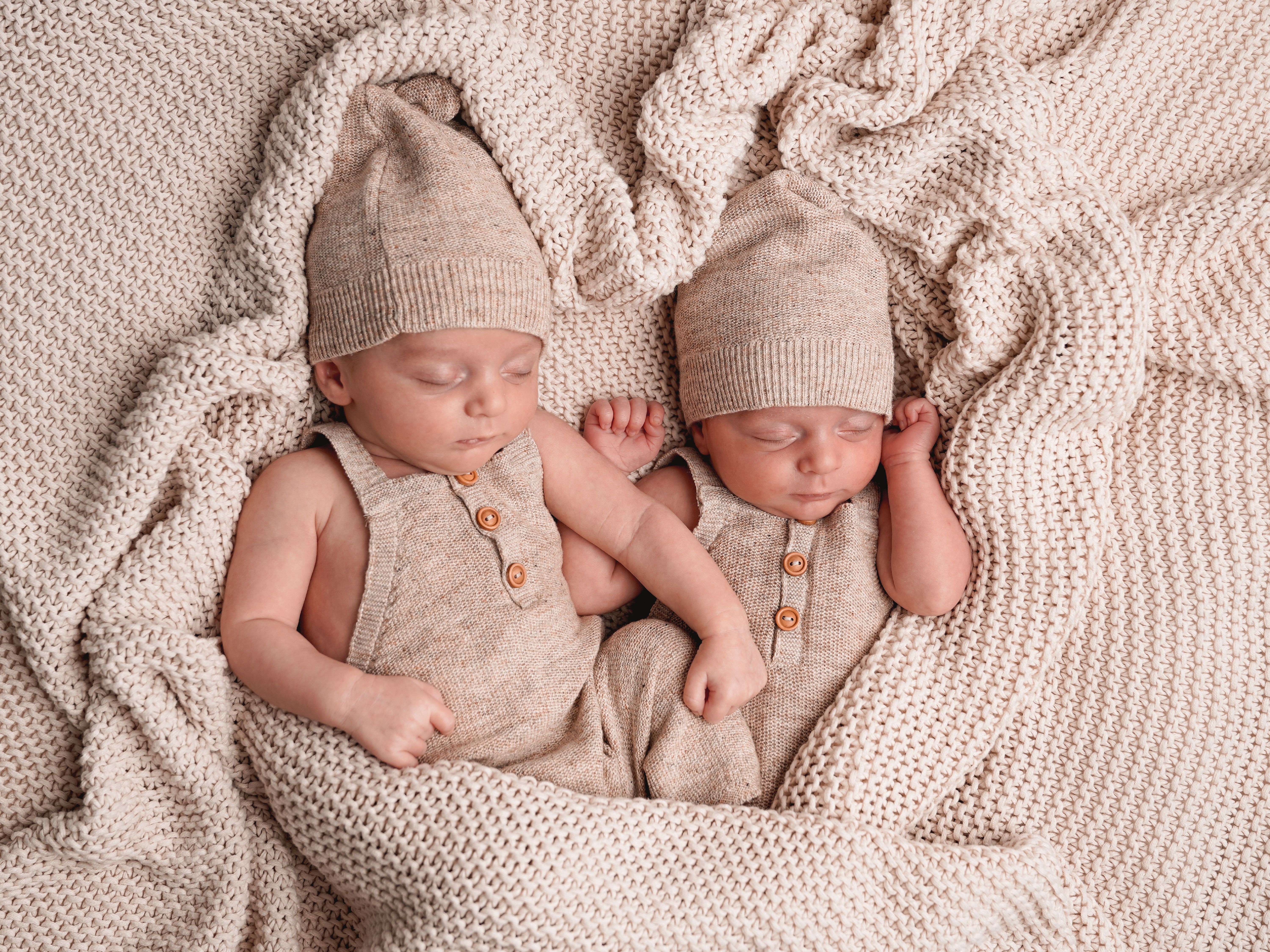 2 Babys mit Mütze liegen auf einer Decke
