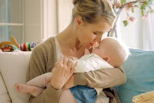 Ein zärtlicher Moment zwischen einer Mutter und ihrem Baby, in dem die Mutter sanft die Stirn des Babys küsst.