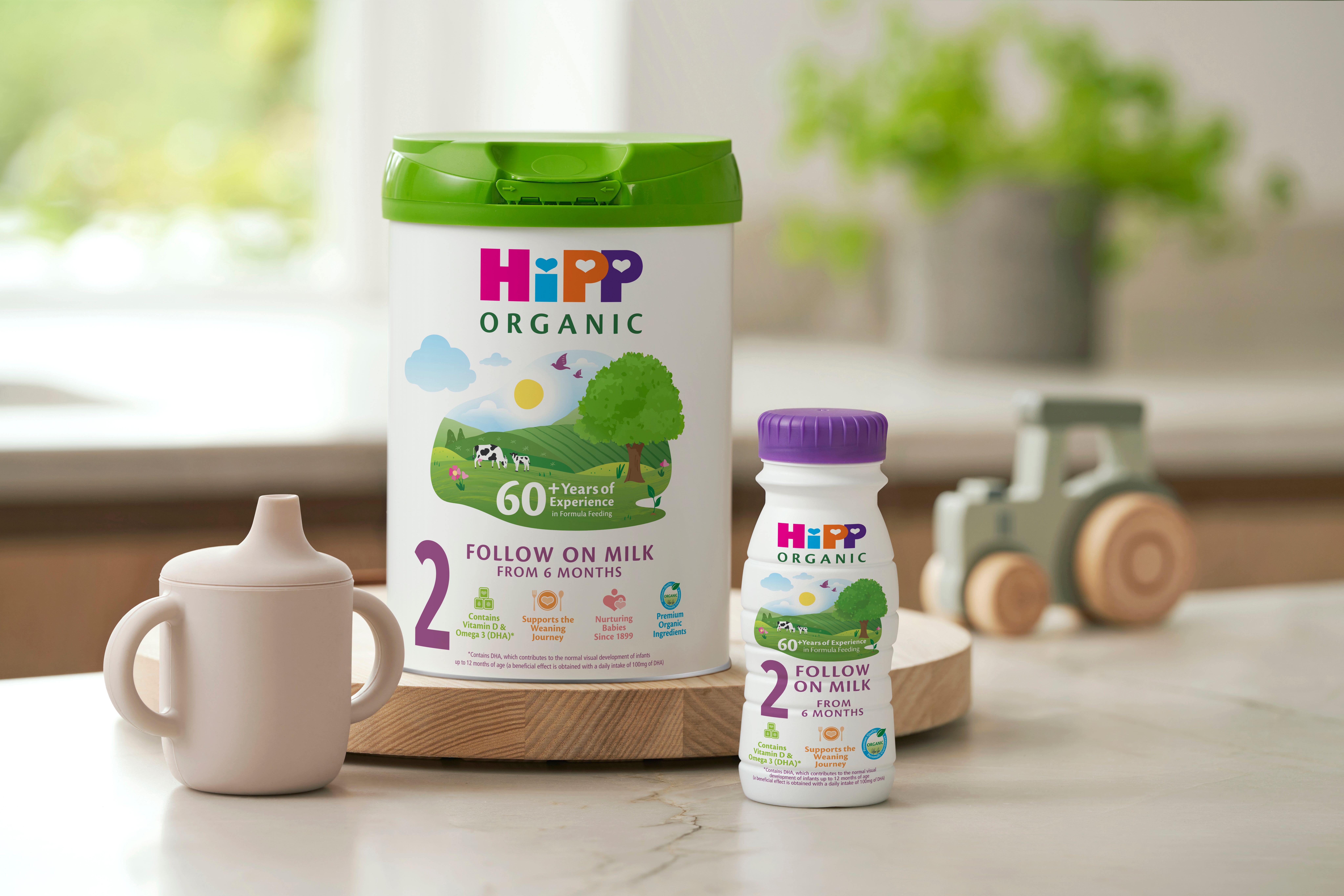 HiPP Organic follow on milk powder tin and ready to feed bottle on a kitchen worktop next to a sippy cup