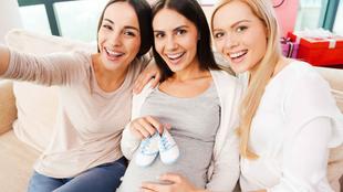 Drei Frauen, von denen zwei Babyschuhe in der Hand halten, lächeln und posieren für ein Selfie.