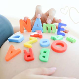 Eine Hand, die bunte Buchstaben- und Zahlenblöcke auf eine Fläche legt, auf der das Wort "NAME" deutlich sichtbar ist.