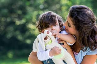 Ein zärtlicher Moment zwischen einer Frau und einem kleinen Kind, wobei das Kind ein Plüschtier in der Hand hält und die Frau das Kind genau beobachtet.