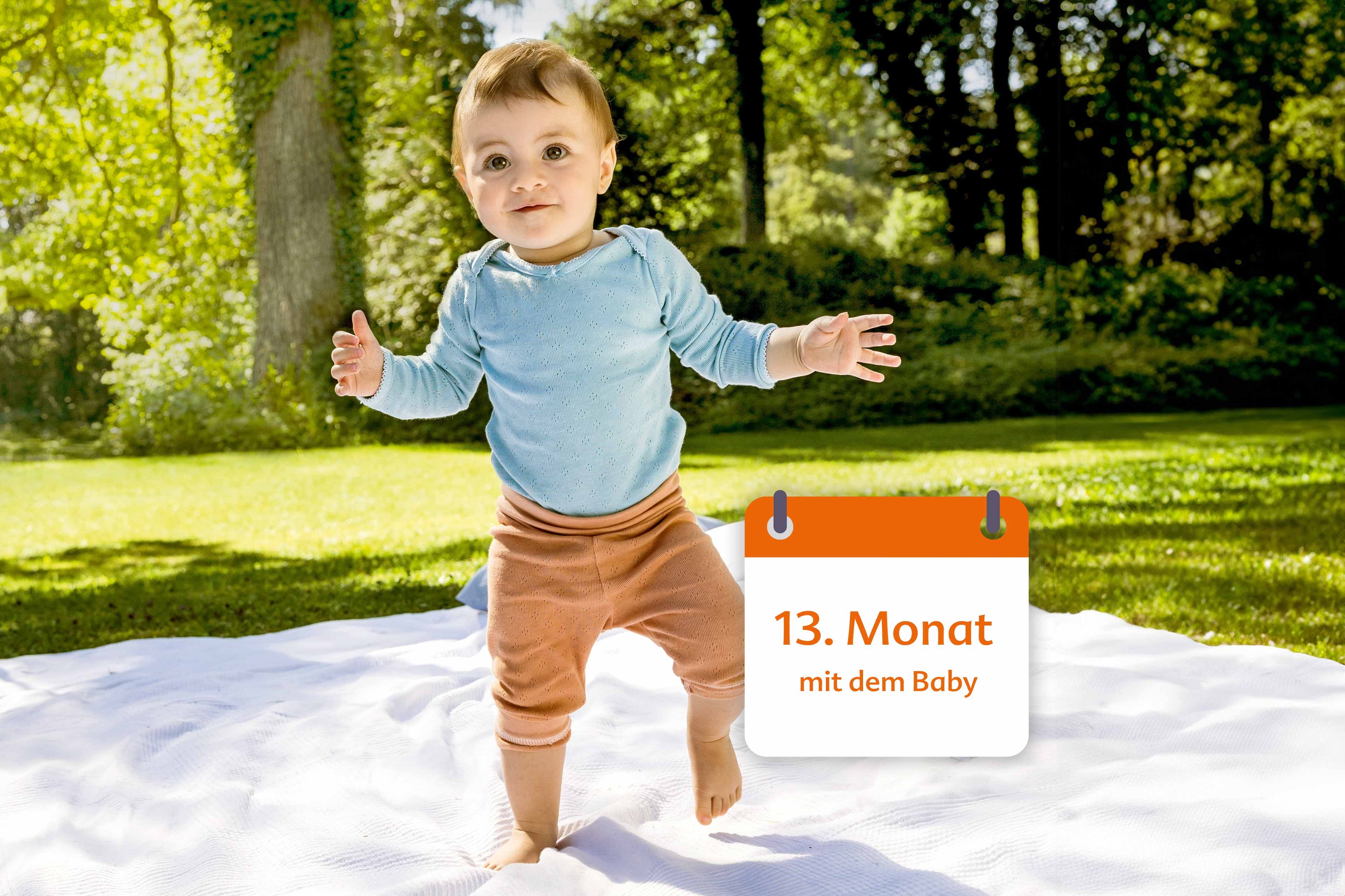 Ein vermutlich 13 Monate altes Baby, das auf einer Decke im Freien steht, mit Grünpflanzen im Hintergrund.