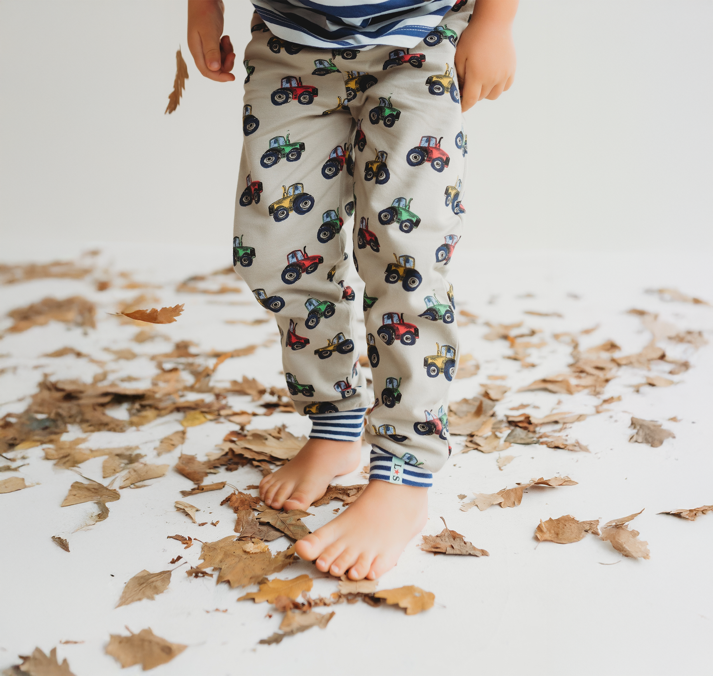 Little boy wearing stone tractor joggers walking through leaves