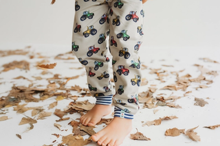 Little boy wearing stone tractor joggers walking through leaves